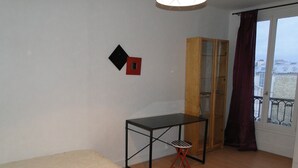 A room with a bed, a small table, a cabinet, and a window with curtains. - Apartment Trocadero (Paris)