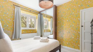 A bedroom with a bed, a large mirror, and yellow floral wallpaper. - GuestReady - Lovely haven with a private garden (London)