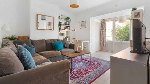 A modern living room with a sofa, coffee table, and a flat-screen TV. - GuestReady - Lovely haven with a private garden (London)