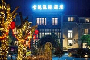 A building with illuminated signage, a well-maintained garden with trees, and a clear night sky. - Baolong Yugang Hotel (Shanghai)