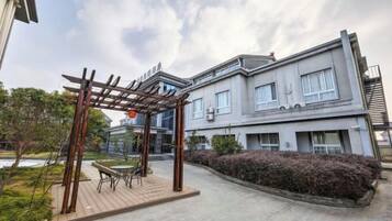 A residential building with a covered outdoor seating area, a balcony, and a well-maintained garden.