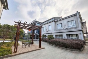 Un edificio residenziale con una zona salotto esterna coperta, un balcone e un giardino curato.