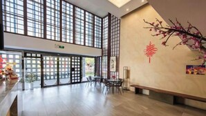 Un hall d’entrée spacieux avec un plafond haut, de grandes fenêtres, un comptoir de réception et un espace salon.