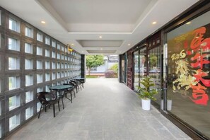 A corridor with a seating area, a glass wall with a decorative design, and a potted plant. - Baolong Yugang Hotel (Shanghai)