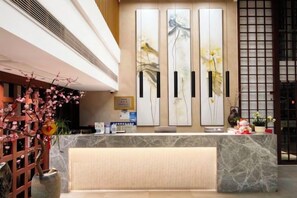 A reception area with a marble counter, a decorative plant arrangement, and a traditional-style wall with vertical elements. - Baolong Yugang Hotel (Shanghai)
