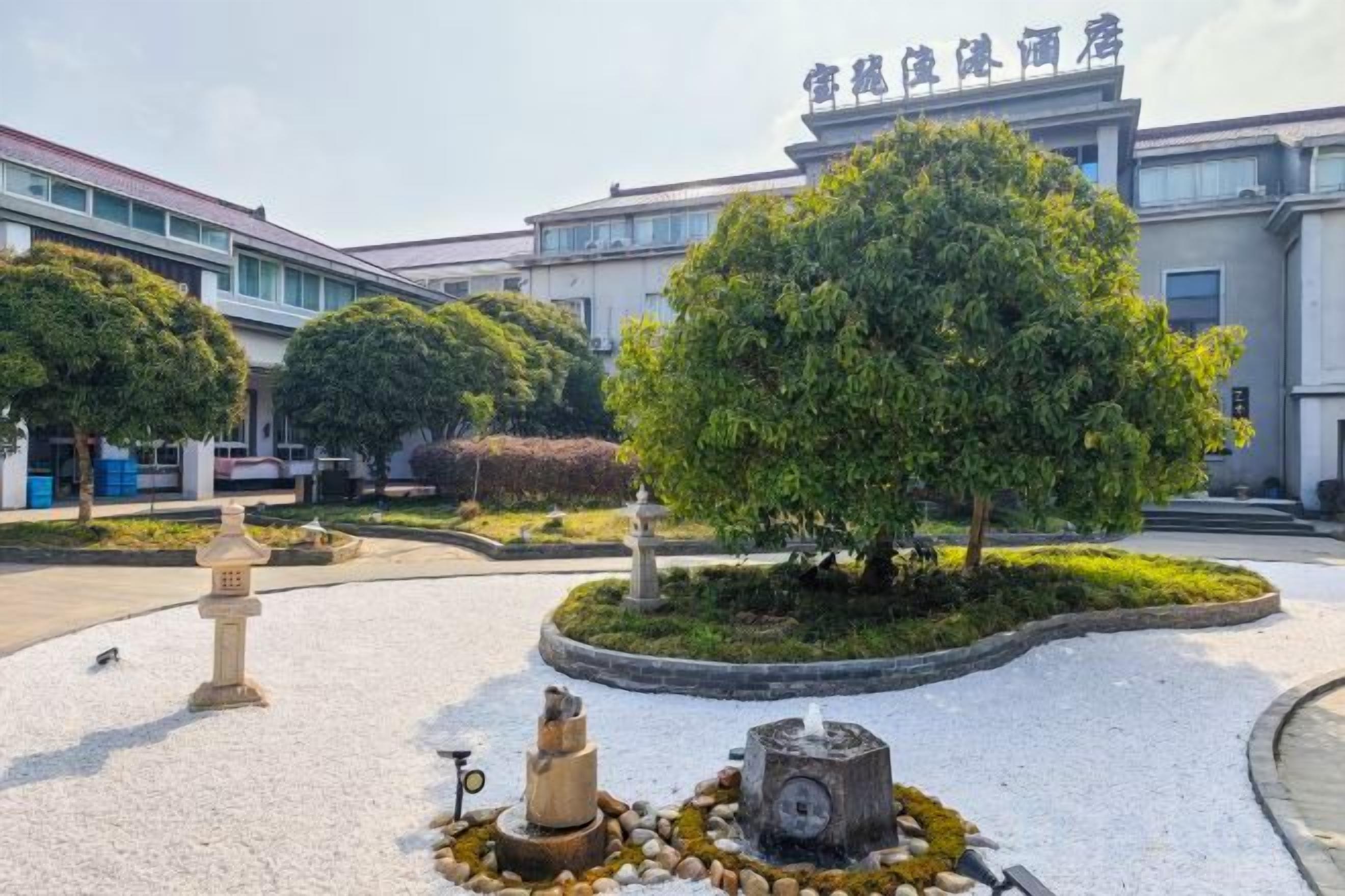 A courtyard with a large tree, a stone lantern, and a fountain.
