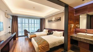 Une chambre d’hôtel avec deux lits, un bureau, une chaise, une grande fenêtre et une salle de bain avec un miroir et un lavabo.