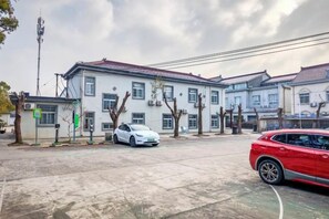 Una strada residenziale con un edificio bianco, un'auto rossa e un'auto bianca parcheggiate davanti.