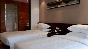 Ein Hotelzimmer mit zwei Betten, einer Holzwand, einem Gemälde und einem durch eine Glastür einsehbaren Badezimmer.