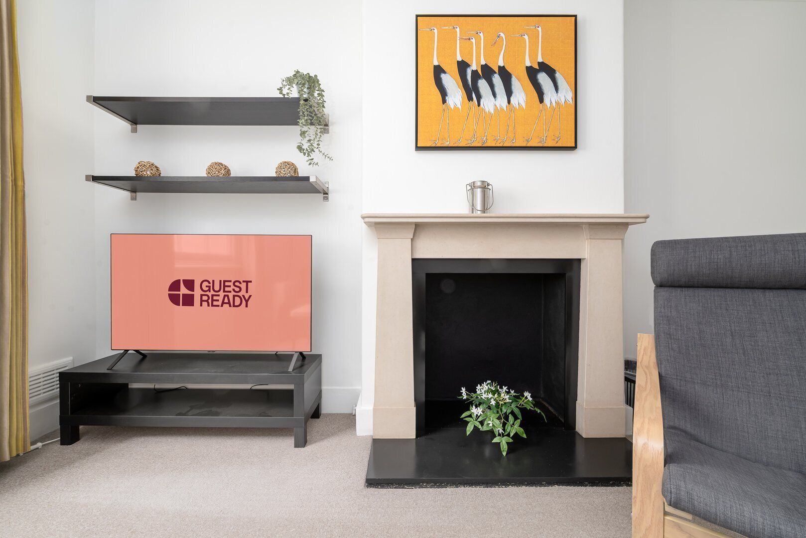 A modern living room with a fireplace, a flat-screen TV displaying "GUEST READY", and a framed artwork of birds.