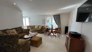 Un salon comprenant un canapé, une table à manger avec des chaises, un téléviseur fixé au mur et une fenêtre avec des rideaux.
