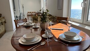 Un coin repas avec une table ronde en bois, dressée pour quatre personnes, entourée de chaises. Un vase rempli de fleurs est posé sur la table, et de grandes fenêtres offrent une vue sur la ville.