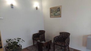 Ein Wohnzimmer mit zwei gemusterten Sesseln, einem kleinen Holztisch, einer Topfpflanze und einem gerahmten Bild an der Wand.