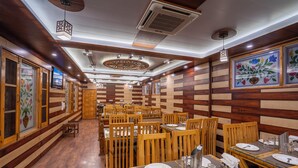 A restaurant with wooden walls and ceiling, featuring a long counter with tables and chairs. - Bombay Residency (Pahalgam)