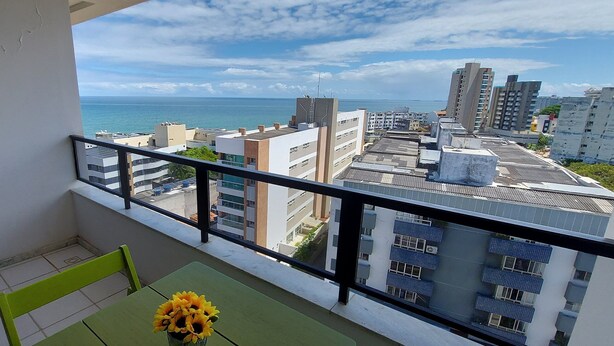 A balcony with a view of the sea, a table with a vase of sunflowers, and a hanging object. - CORVE0104 - Marítima Residence (Salvador)