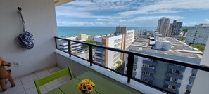Un balcón con vista al mar, una mesa con un jarrón de girasoles y un objeto colgante.