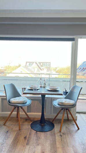 Un coin repas avec une table et deux chaises, donnant sur une maison et sur l’eau.