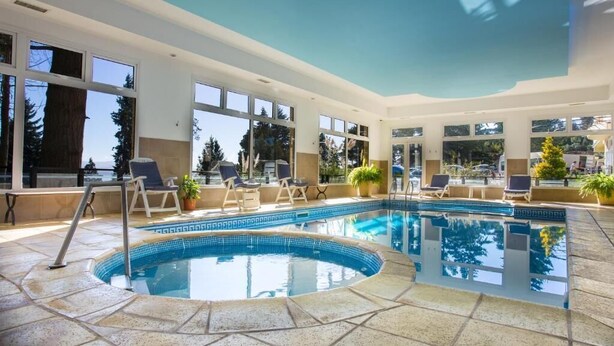 Une piscine intérieure moderne avec des parois en verre transparent, des chaises longues et des plantes en pot.