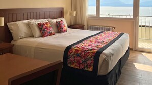 Une chambre d’hôtel avec un grand lit, un bureau et une vue sur la mer.