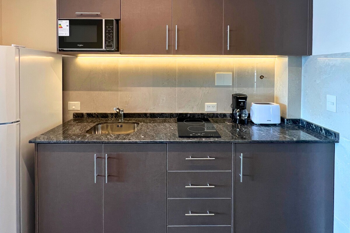 A modern kitchen with dark cabinets, a stainless steel sink, a microwave, a toaster, and a built-in oven.