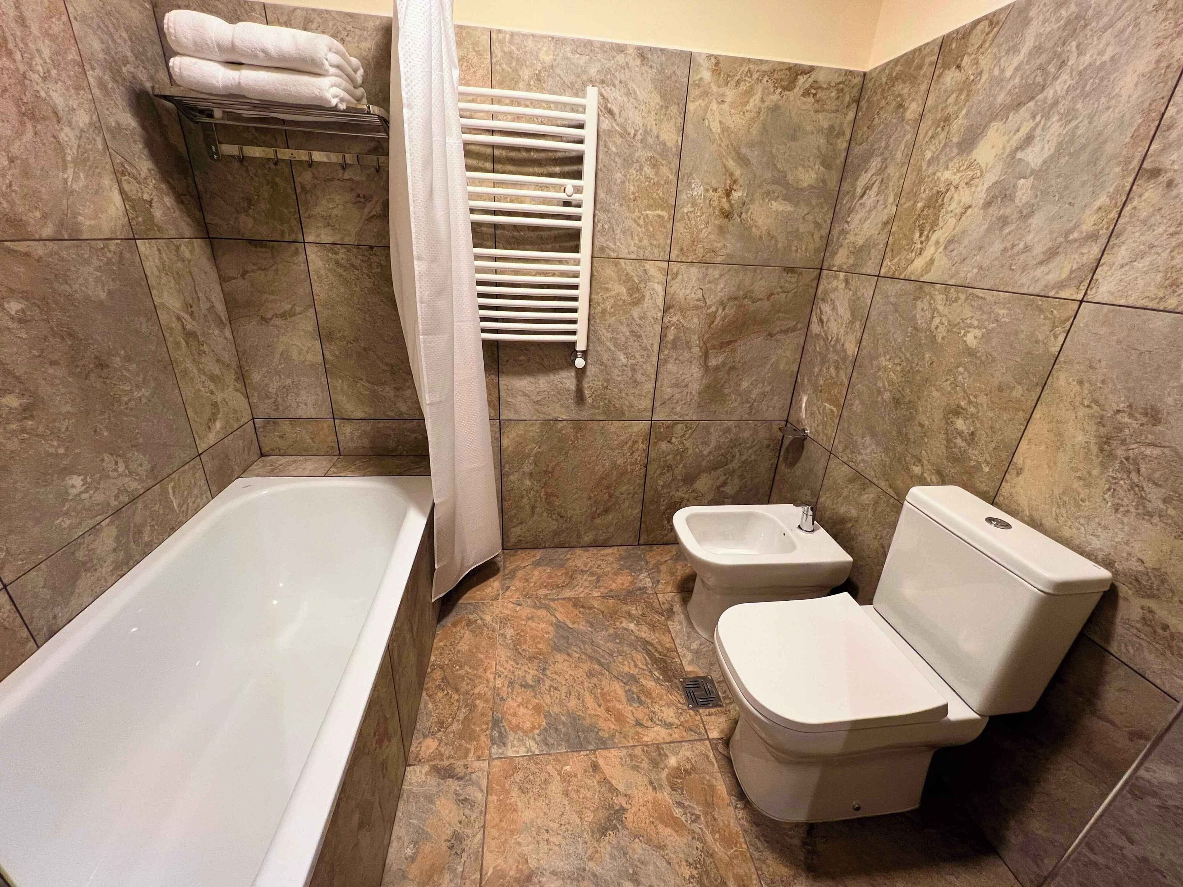 A bathroom with a bathtub, a toilet, a bidet, and a towel rack with towels.