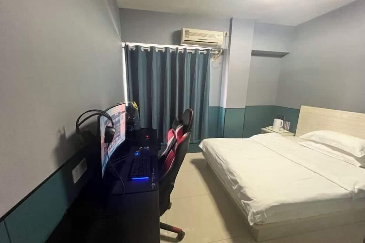 Camera d'albergo con un letto, una scrivania con un computer, una sedia, una tenda e un condizionatore d'aria.
