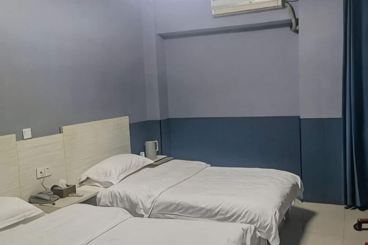 Una camera d'albergo con due letti, un comodino, una lampada e una finestra con tenda.