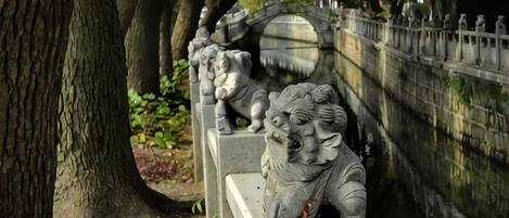 Eine Steinkonstruktion mit Löwenstatuen, umgeben von Bäumen und einem Wasserlauf.