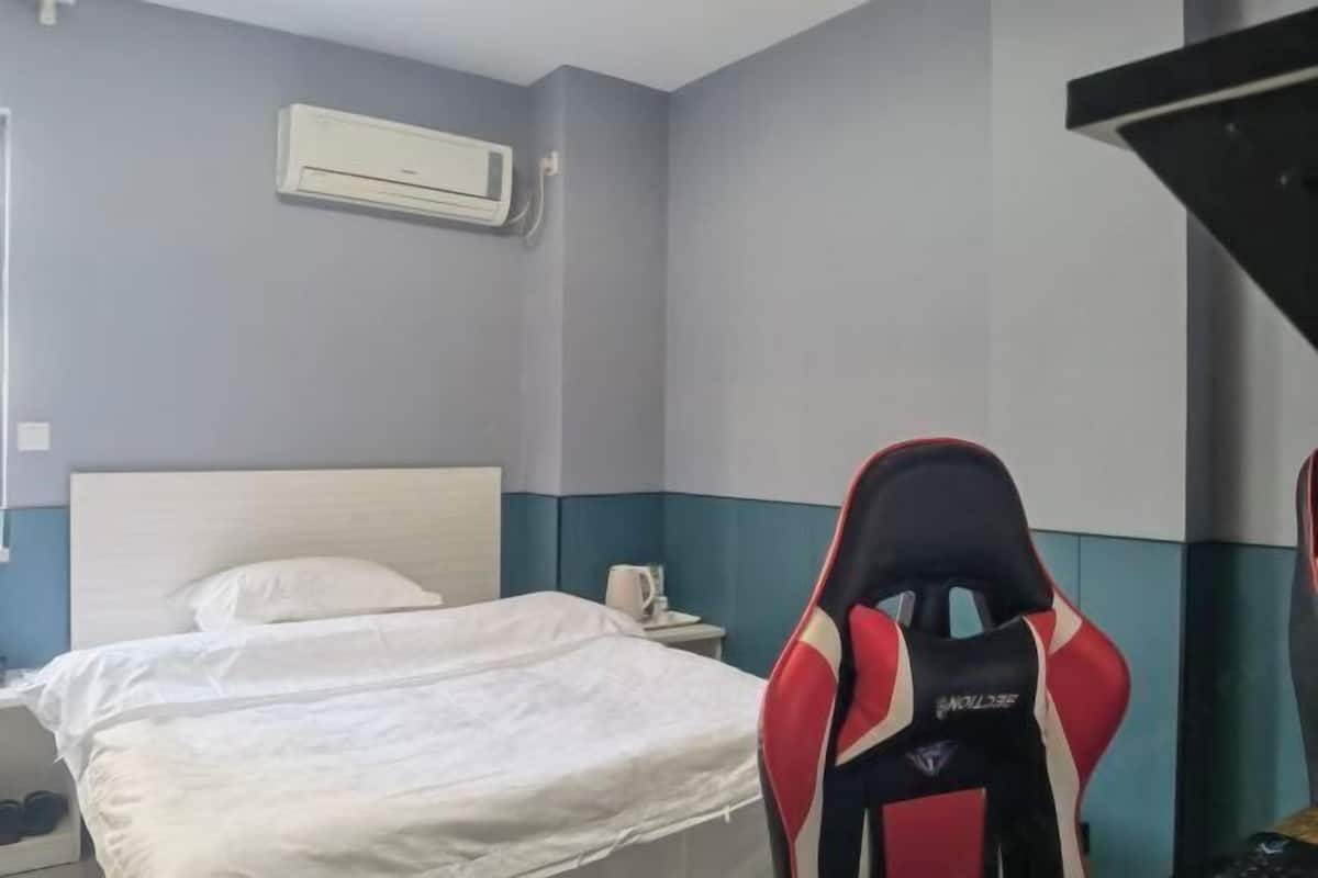 Una camera d'albergo con un letto, un comodino, un condizionatore d'aria e una poltrona da gaming.