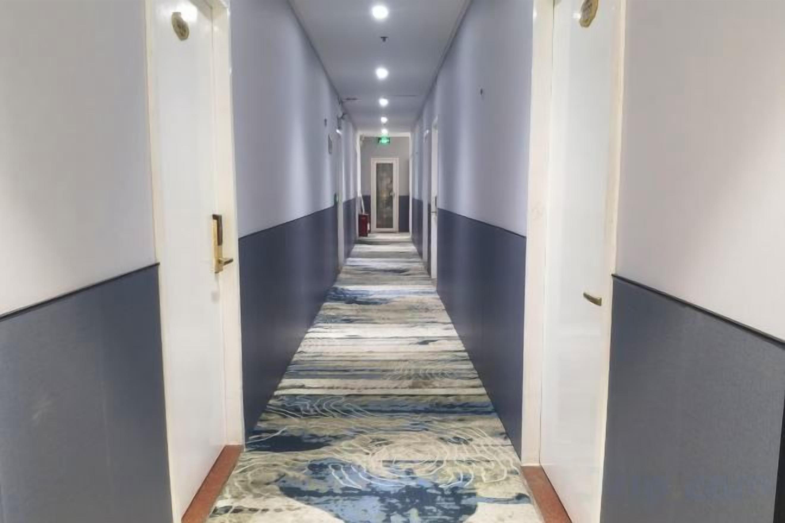 A long, narrow hotel corridor with doors on both sides and a patterned carpet.