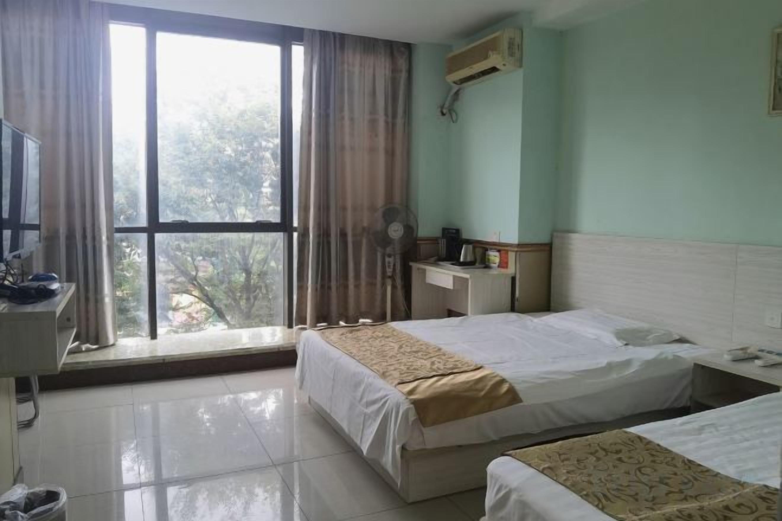 Une chambre d’hôtel avec deux lits, un bureau, une chaise, une fenêtre avec des rideaux et un appareil de climatisation.