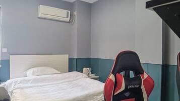 Une chambre d’hôtel équipée d’un lit, d’une table de chevet, d’un climatiseur et d’un fauteuil de jeu vidéo.