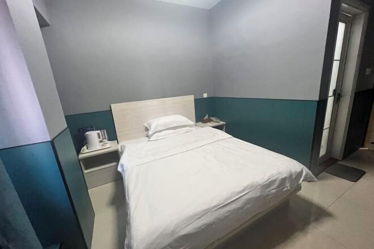 A hotel room with a bed, a nightstand, a white pillow, and a white mug.