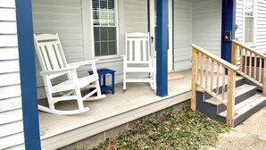 A porch with white rocking chairs and a small table, wooden steps, and a blue door. - Charming Coastal Cape Cod w/ King Bed, Bikes, & Game Room near Downtown Beach (Vermilion)