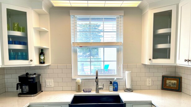 A kitchen with white cabinets, a black coffee maker, a window with blinds, and a countertop with various items. - Charming Coastal Cape Cod w/ King Bed, Bikes, & Game Room near Downtown Beach (Vermilion)