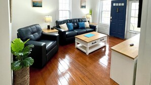 A spacious living room with a black leather sofa, a wooden coffee table, and a large window. - Charming Coastal Cape Cod w/ King Bed, Bikes, & Game Room near Downtown Beach (Vermilion)