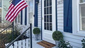 A house with a front porch, a welcome mat, and an American flag. - Charming Coastal Cape Cod w/ King Bed, Bikes, & Game Room near Downtown Beach (Vermilion)