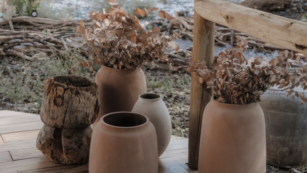 A wooden deck with terracotta pots containing dried plants, a rustic wooden fence, and a pathway leading into a wooded area. - UNAI Atacama Luxury Tents (San Pedro de Atacama)