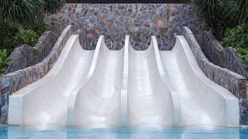 Une piscine dotée de quatre toboggans, entourée d’un mur de pierre et de plantes tropicales.