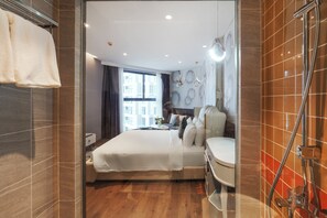 Quarto de hotel moderno com uma cama grande, banheiro com chuveiro e vista da cidade.