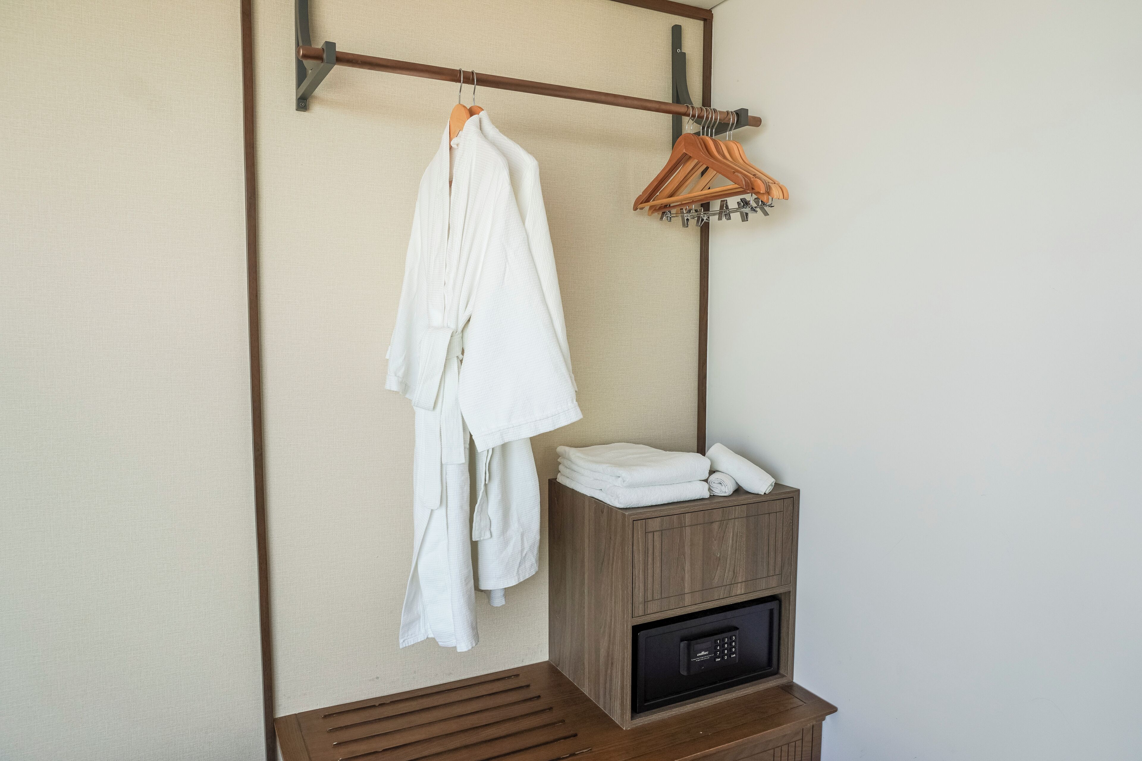 A bathroom with a towel rack holding several white towels, a wooden cabinet with folded towels, and a black electronic device on a wooden counter.