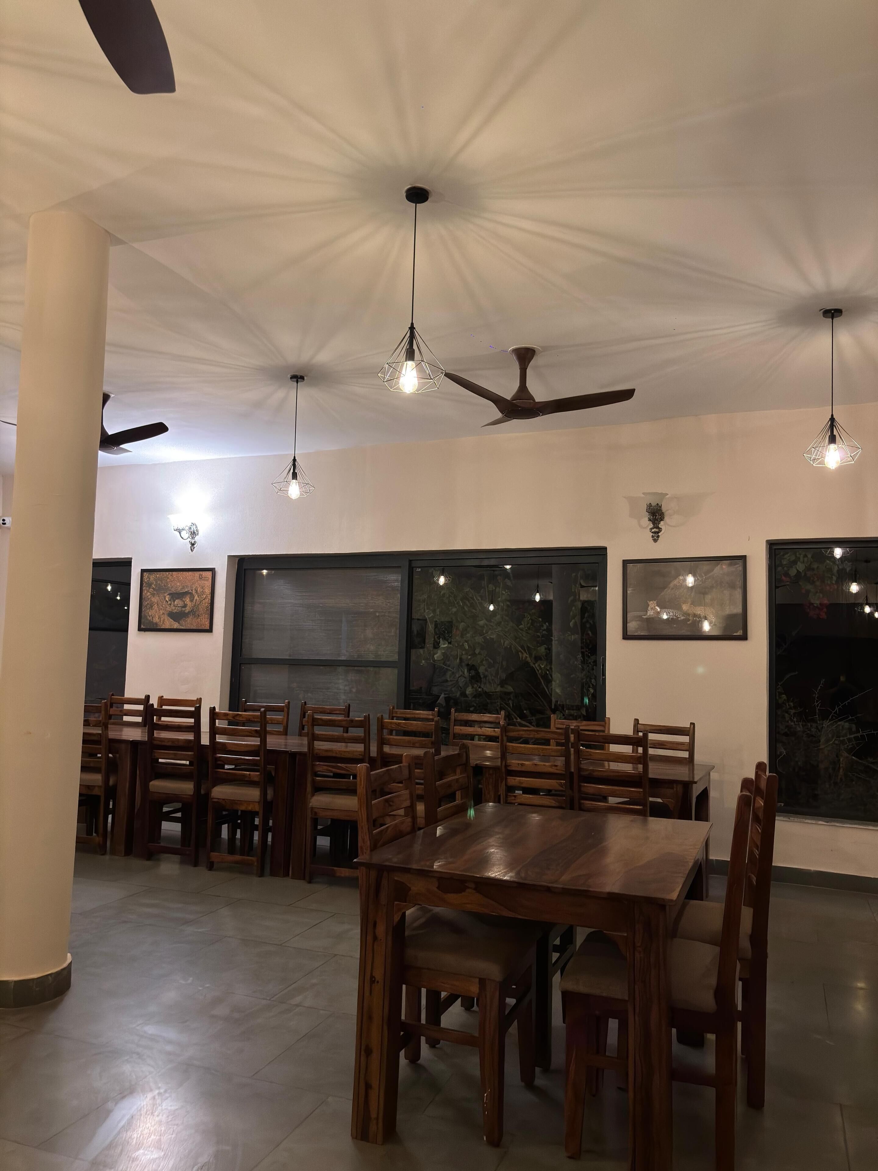 Interior de restaurante con mesas y sillas de madera, ventiladores de techo, lámparas colgantes y cuadros en las paredes.