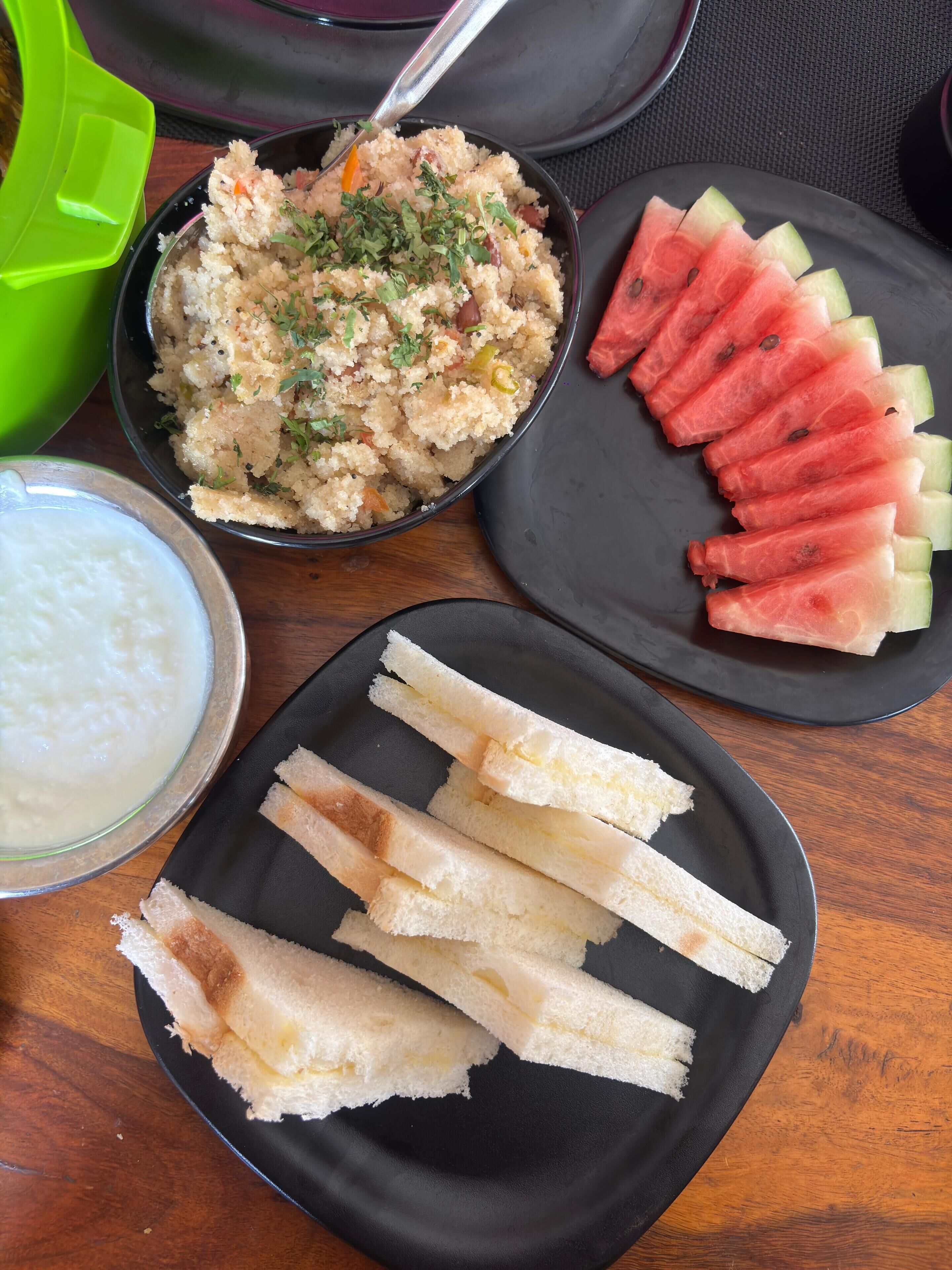 Une table avec un saladier de salade de couscous, des tranches de pastèque, une assiette de gressins et un bol de yaourt.