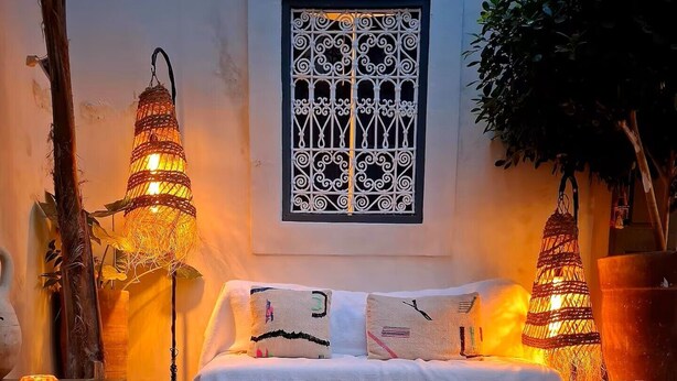 A bedroom with a bed, two wall-mounted lamps, a window with decorative bars, and a small pool in front.