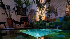 A pool area with a checkered floor, surrounded by potted plants and a mosaic bowl.