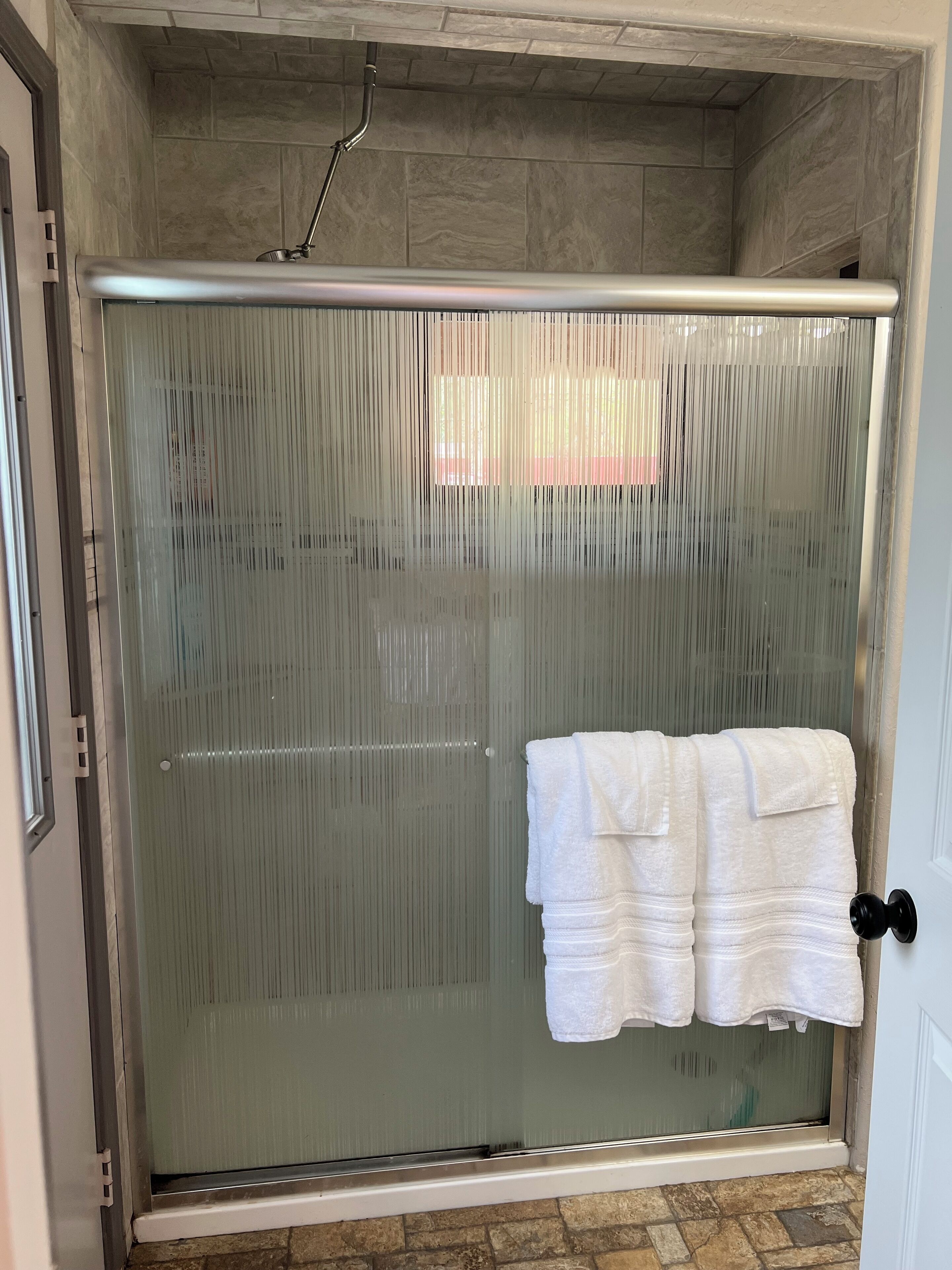 A shower enclosure with a glass door, a towel rack with two white towels, and a showerhead.