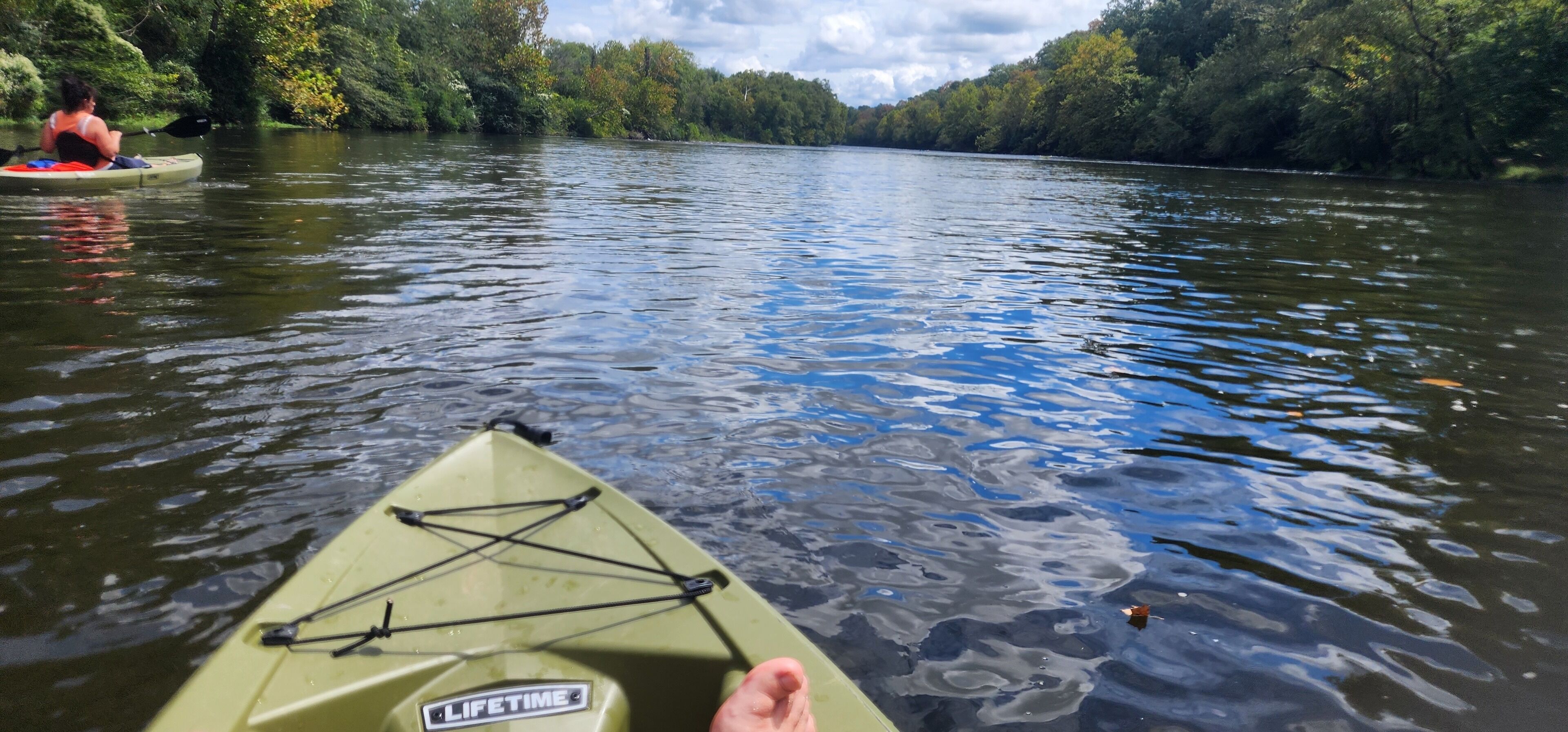A kayak on a calm river with trees on both sides.