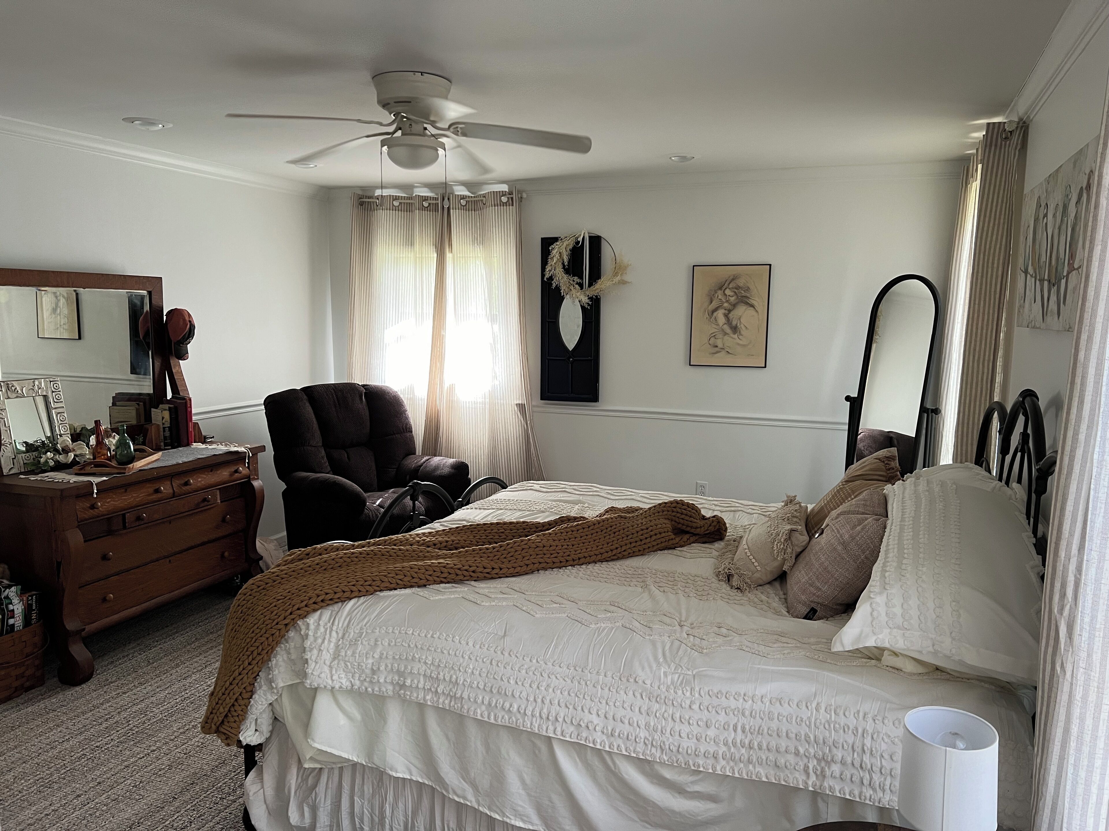 A bedroom with a bed, a chair, a dresser, a ceiling fan, and a mirror.