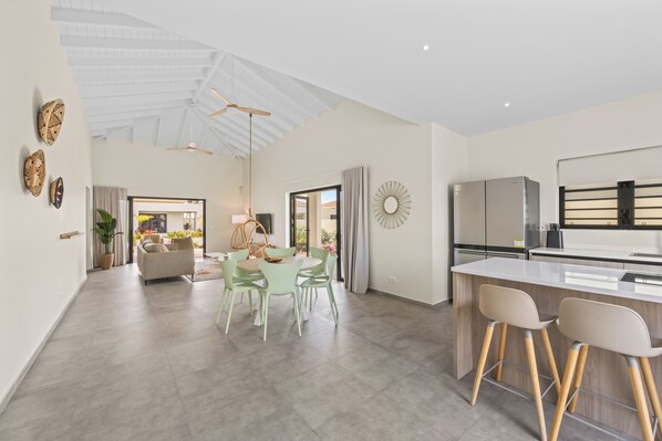 A spacious living area with a high ceiling, a dining table with chairs, a kitchen with modern appliances, and a view through an open doorway. - Infinity Blue villa with private pool at Mambo Beach (Willemstad)