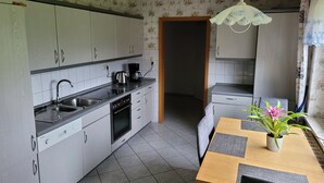 A compact kitchen with a sink, stove, and coffee maker, a dining table with chairs, and a potted plant. - Vacation apartment with garden in Drochtersen (Drochtersen)